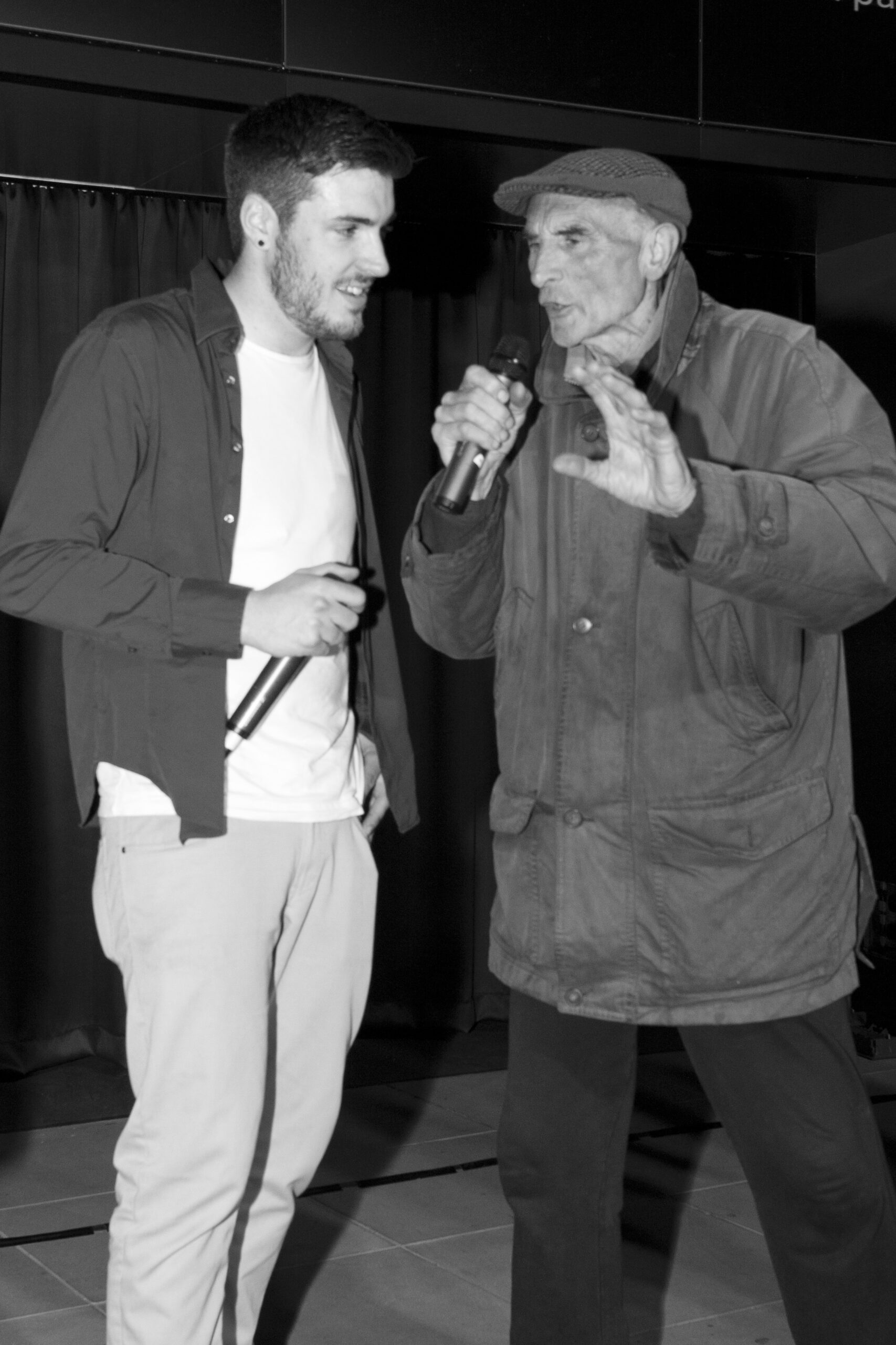 Joe and older man in black and white holding microphones chatting 